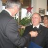 Der Landrat steckt Msgr. German Fischer die Ehrenmedaille in Gold an und überreicht Urkunde und große Medaille